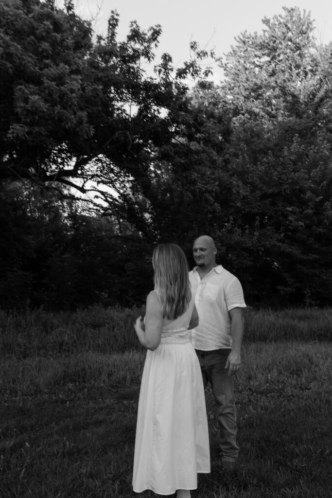 Black and white photo of a couple standing, looking at each other during an engagement session at Wildcat Bluff Recreation Area in Vinton, IA.